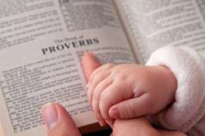 Baby Holding Dad’s Finger on Bible